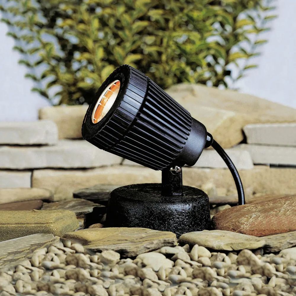 Black outdoor spotlight with ribbed head, circular lens, mounted on pedestal base