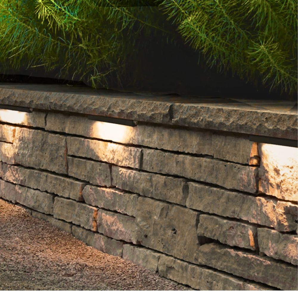 Outdoor hardscape LED light fixture with warm glow along the stone wall