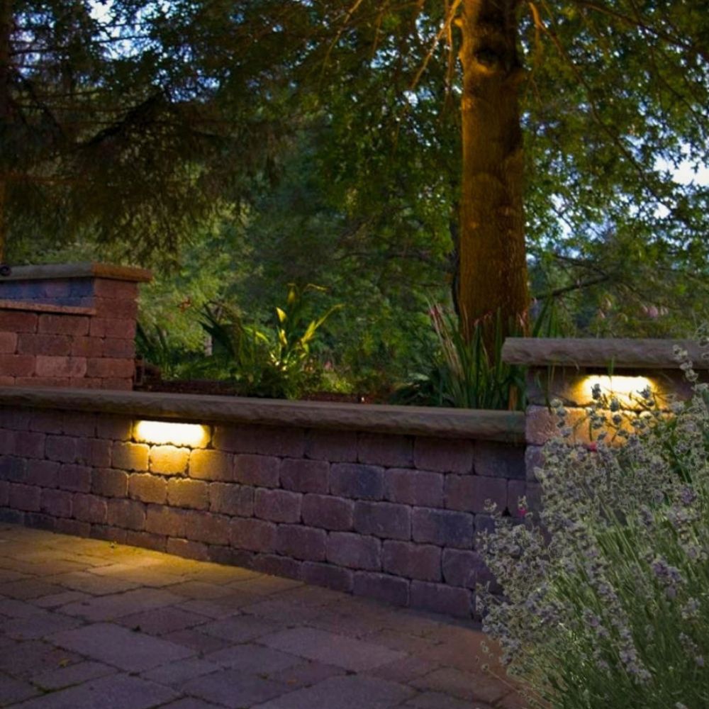 Warm hardscape LED lights illuminating a brick retaining wall in a garden