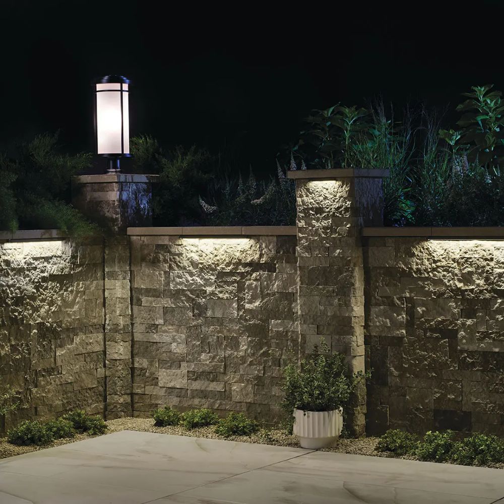 Textured bronze 12V hardscape LED light glowing upward on outdoor wall