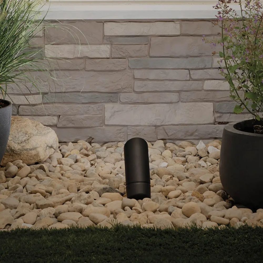 Black outdoor landscape LED accent light in pebble landscaping near stone wall