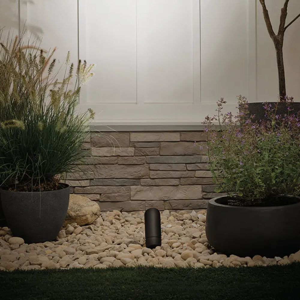 Black outdoor landscape LED accent light between planters along a gravel walkway