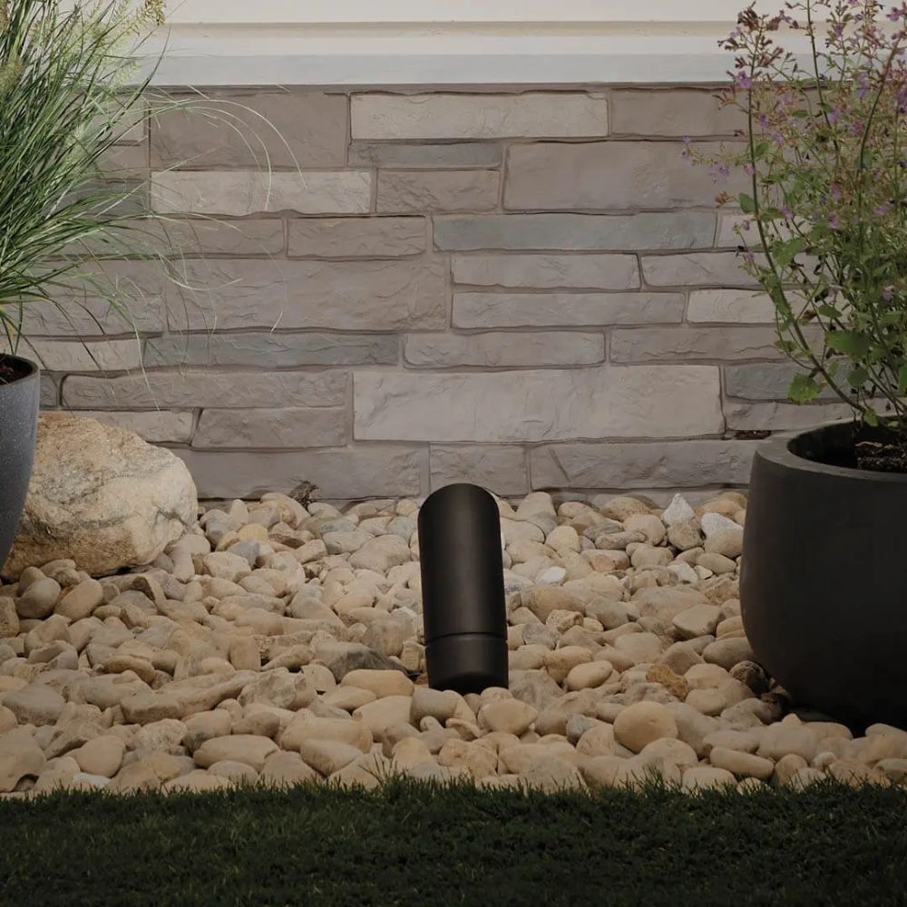 Black landscape LED accent light in a pebble bed against a stone wall