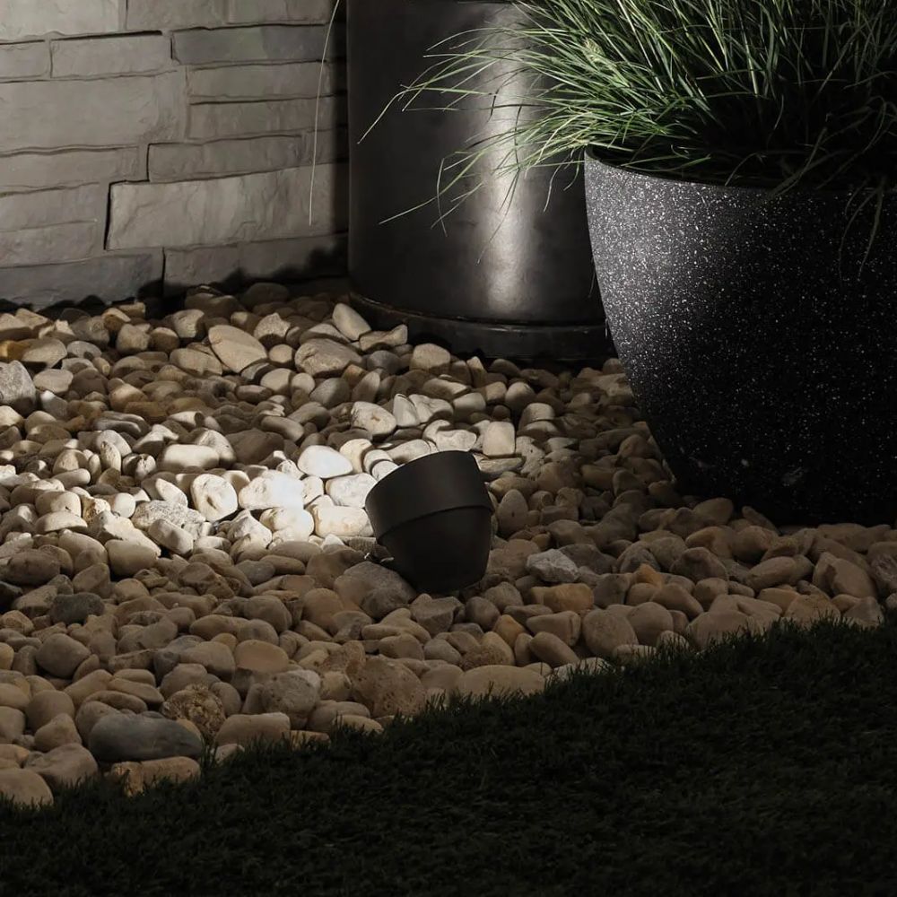 Black LED landscape accent light with angled head installed in garden gravel near grass