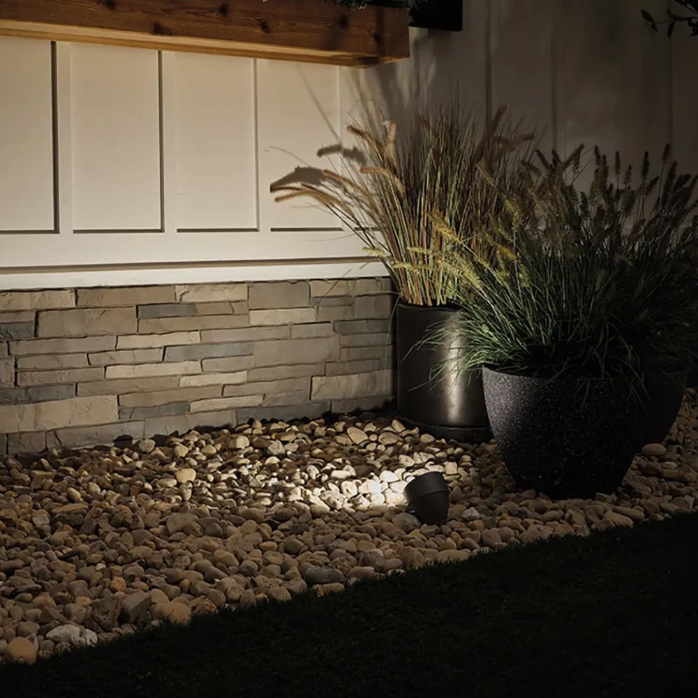 Kichler textured black LED landscape accent flood light casting light on gravel and plants