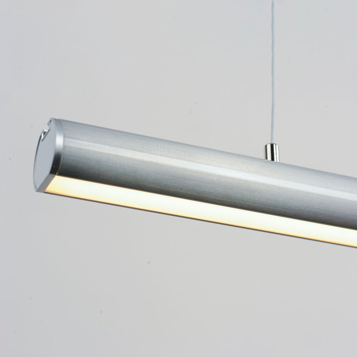 Brushed satin aluminum linear pendant with cylindrical shade and warm light beam