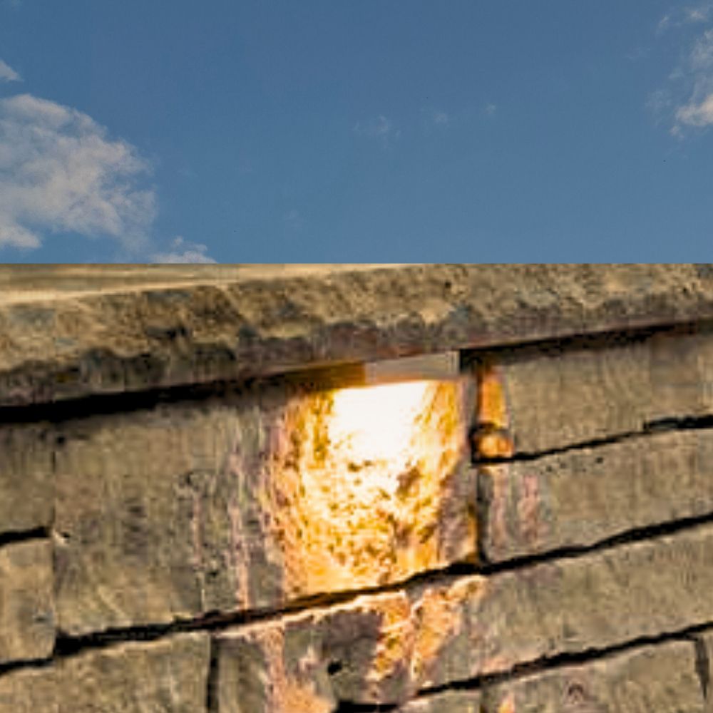 Brass 12V LED hardscape light with warm glow on stone wall