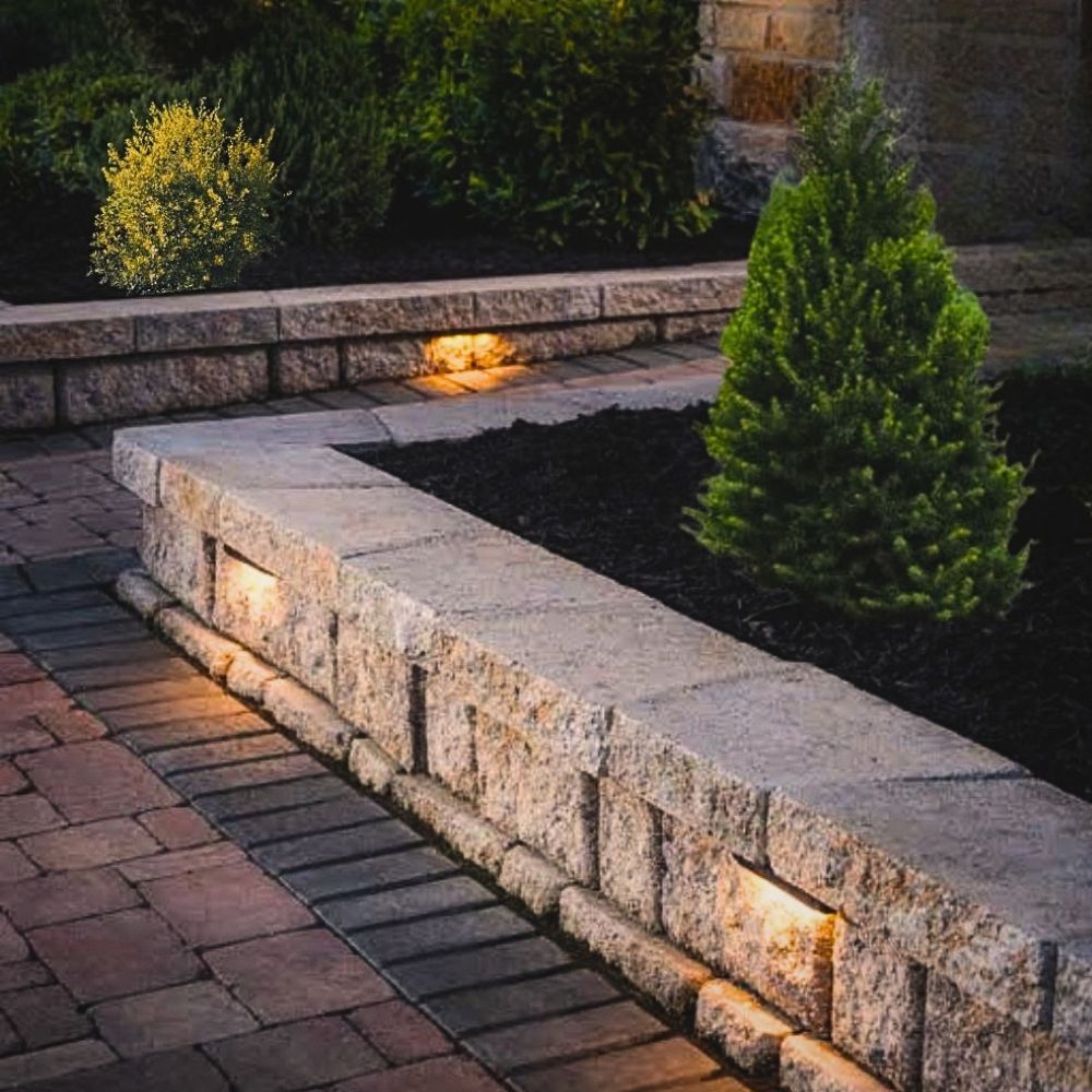 Outdoor hardscape LED light in sand aluminum housing, installed in stone wall with warm glow