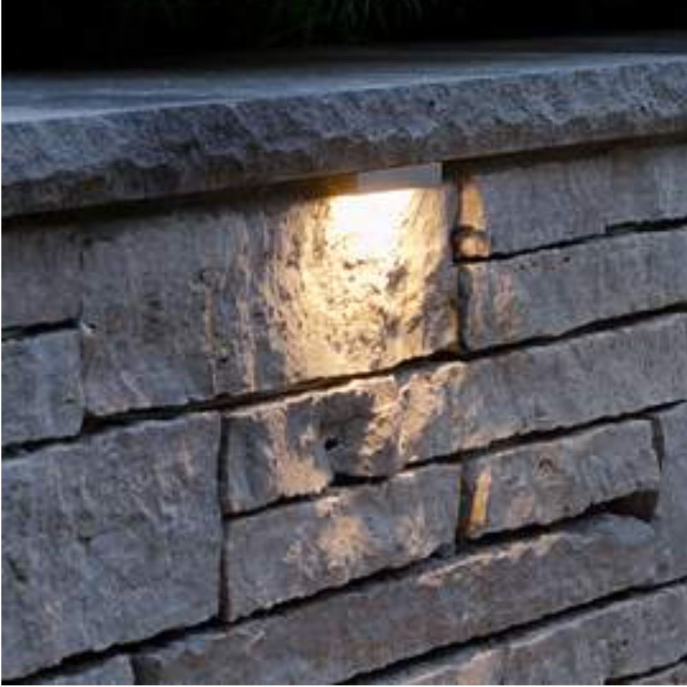 Warm 12V LED hardscape light glowing in a stone wall, mounted between bricks