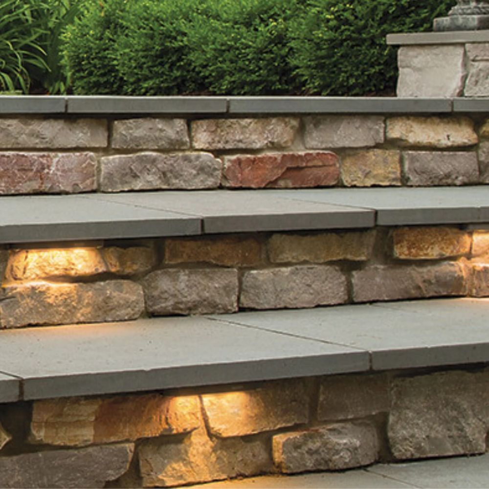 Bronze 12V LED hardscape light installed along stone wall with warm glow