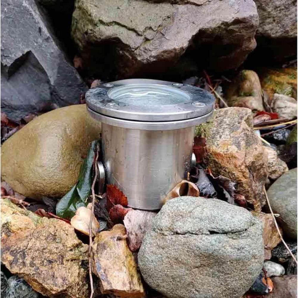 Stainless steel underwater LED light set in rocky landscaping with visible round head