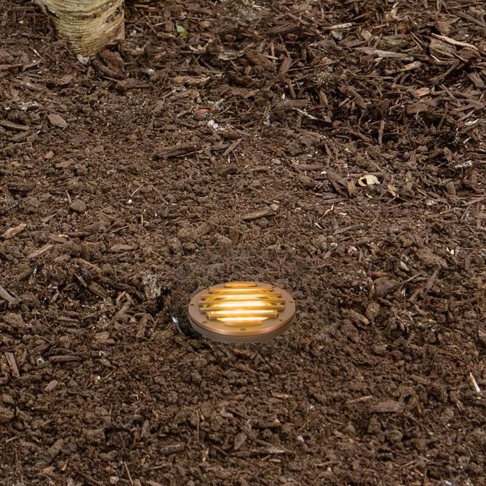 In-ground LED well light with glowing brass round cover in dark soil
